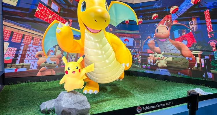 Heldere etalage met gigantische Dragonite en Pikachu figuren binnen een Pokémon Centre.