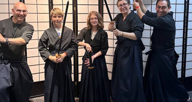 Bezoekers in zwarte hakama poseren met samuraizwaarden in een dojo.