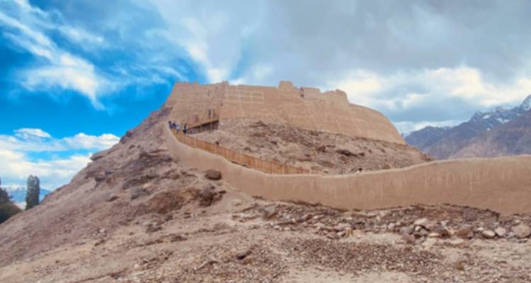 Ruines de forteresse en terre perchées sur une colline rocheuse avec un sentier en zigzag menant vers le haut.