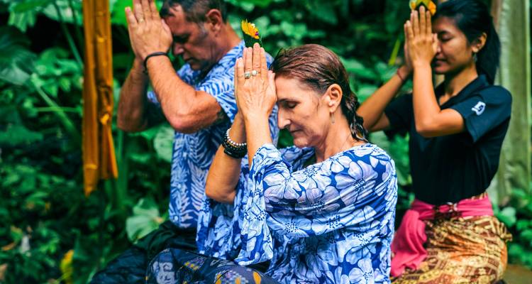 Drie reizigers nemen deel aan een Balinees gebedsritueel in een weelderige jungle omgeving, met handpalmen tegen elkaar gedrukt in meditatie.