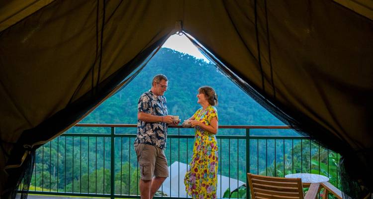 Een stel geniet van koffie in een tent met uitzicht op met jungle bedekte bergen.
