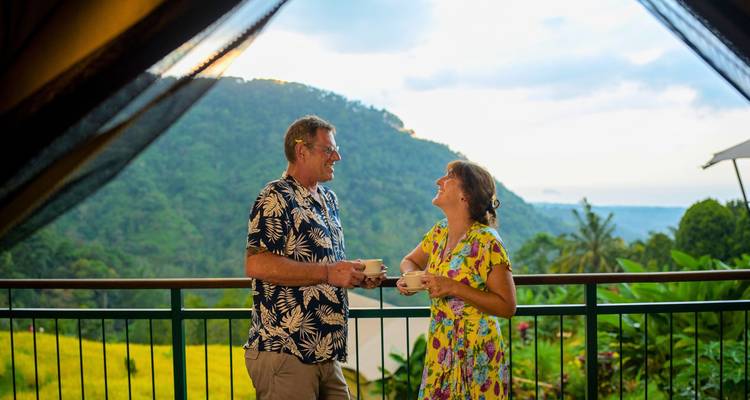 Glimlachend stel geniet van koffie op een balkon met uitzicht op groene rijstterrassen en tropische heuvels in Bali.