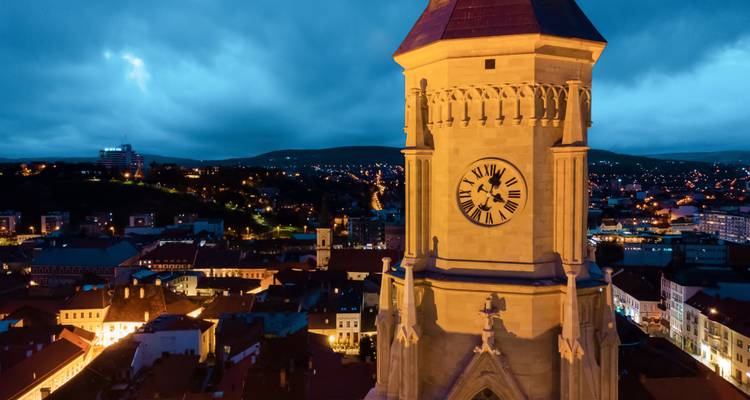 Tour d'horloge illuminée s'élève au-dessus d'un paysage urbain au crépuscule avec des nuages bleus orageux.