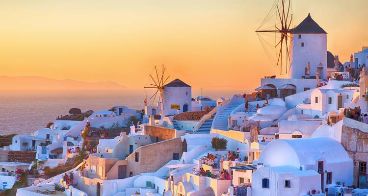 De zonsondergang baadt de witgekalkte huizen en iconische windmolens van Santorini in warm gouden licht met uitzicht over de Egeïsche Zee.