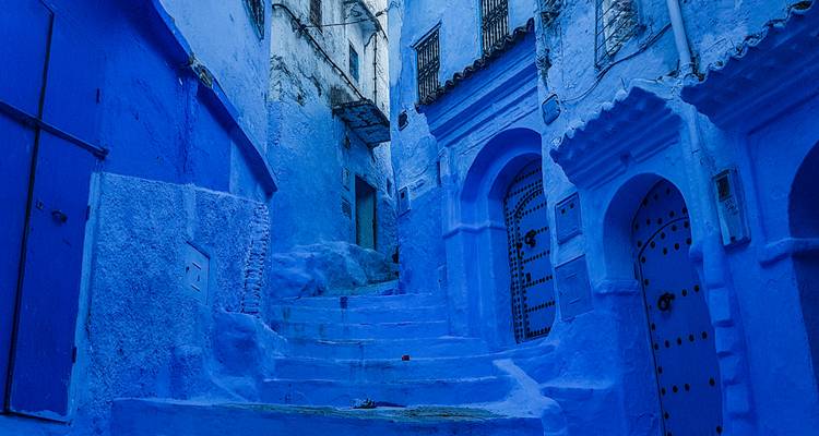 Narrow alley of Chefchaouen painted entirely in vivid shades of blue with arched doorways.