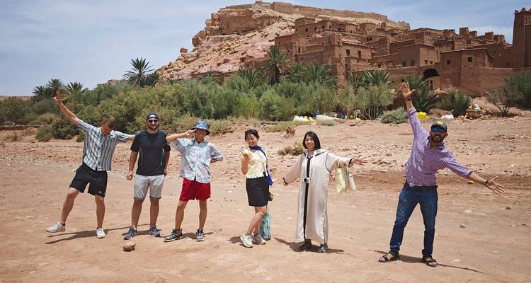 Happy travelers striking poses in front of historic desert fortress under sunny skies.
