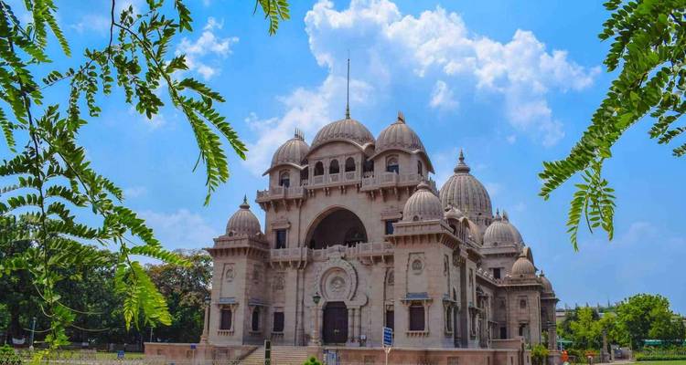 Majestueuze Belur Math tempel met koepels omlijst door groen gebladerte tegen blauwe hemel