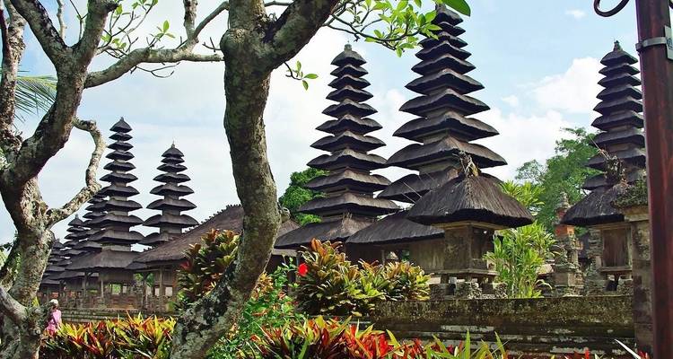 Vista a través de ramas de árboles de altos techos de templo meru similares a pagodas en Bali