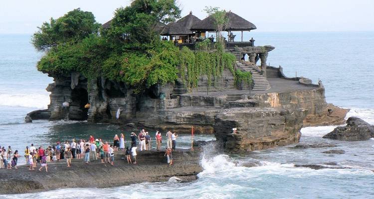 Multitudes visitando el templo marino de Tanah Lot encaramado en un afloramiento rocoso entre olas que rompen