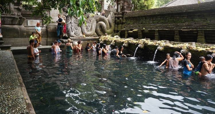 Peregrinos bañándose en la piscina sagrada del templo de agua Tirta Empul rodeados de esculturas