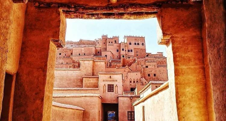Vue à travers une porte en adobe encadrant des bâtiments en briques de terre empilées d'une kasbah.