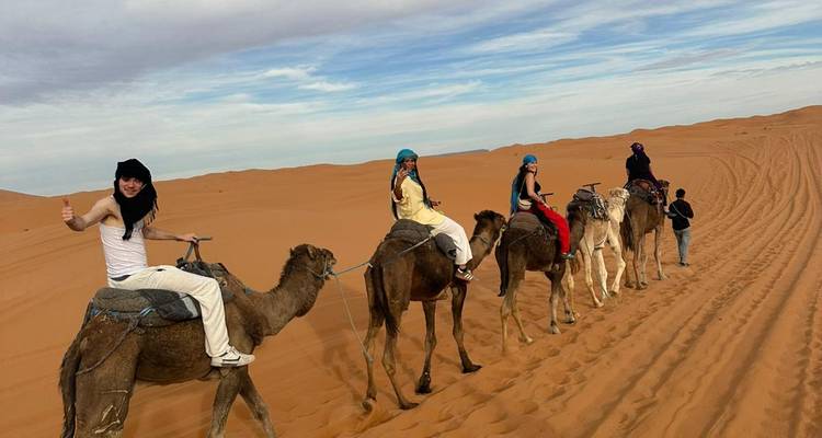 Side view of riders in colorful scarves atop camels moving along a high dune ridge.