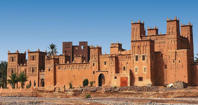 Magnifique kasbah fortifiée avec de multiples tours et des façades ornementées se détachant sur un ciel bleu clair.