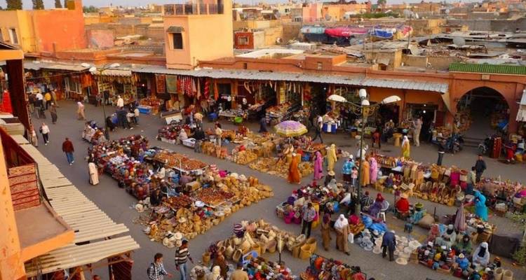 Vue surélevée sur une place de marché en plein air animée avec de nombreux étals colorés et des acheteurs dans une ancienne médina marocaine.