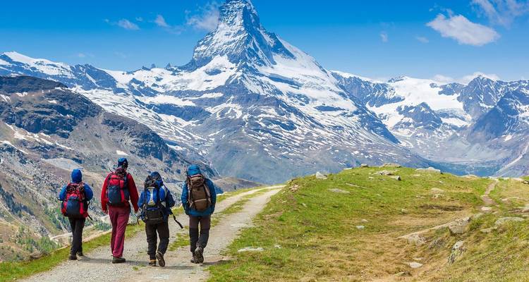 Wandelaars met rugzakken die trekken richting de met sneeuw bedekte Matterhorn onder een heldere blauwe lucht.