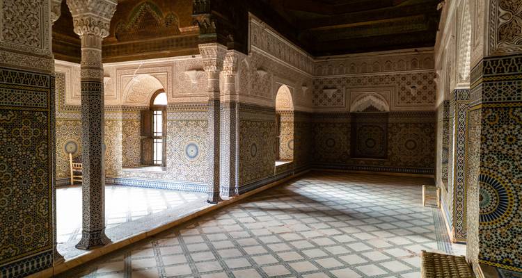 Salle aux carrelages complexes avec des arcs ornementés, des colonnes et des sols à motifs à l'intérieur d'un bâtiment historique marocain.