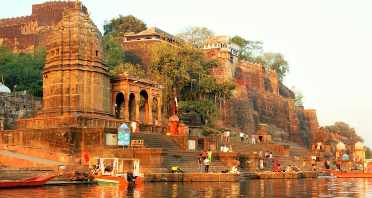 Historische rivierfront ghats en tempels die gloeien in warm licht met lokale bewoners bij de Narmada rivier