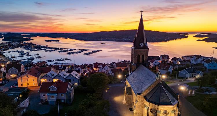Sonnenuntergang über einem schwedischen Küstendorf mit Kirchturm, Jachthafen und leuchtend orangenem Himmel