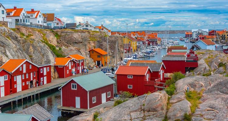 Bunte rote Fischerhütten säumen eine schmale Wasserstraße zwischen Granitfelsen unter einem teilweise bewölkten Himmel
