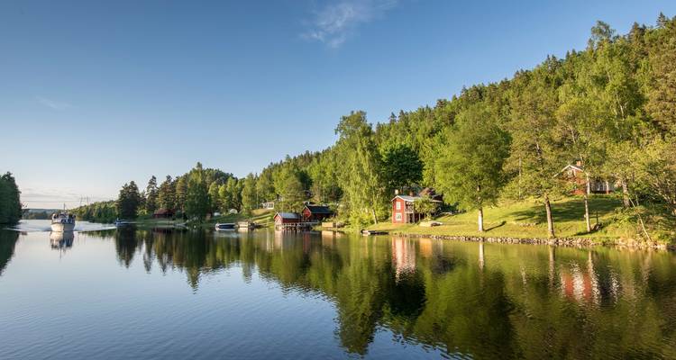 Ruhiges bewaldetes Seeufer mit kleinen roten Hütten, die sich an einem klaren Morgen im spiegelglatten Wasser widerspiegeln
