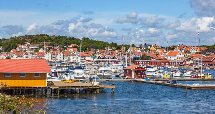 Belebter Yachthafen voller Yachten und Häuser mit orangefarbenen Dächern entlang der Uferpromenade unter blauem Himmel