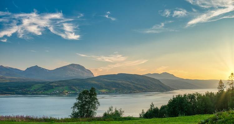 Ruhige Fjordlandschaft bei Sonnenuntergang mit sanften Wolken und weichem goldenem Licht über fernen Bergen