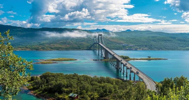 Lange moderne Brücke überspannt türkisfarbene Fjordgewässer unter einem Himmel mit vereinzelten Wolken