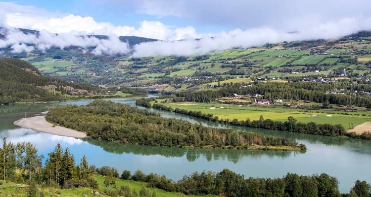 Üppiges Tal mit einem gewundenen Fluss, Flickenteppichfeldern und tiefen Wolken, die sich an grüne Hügel schmiegen.
