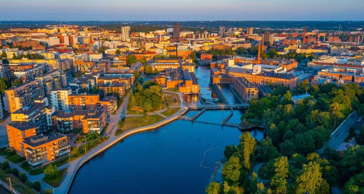 Luftaufnahme von Tampere bei Sonnenuntergang mit roten Backsteinfabriken, Uferpromenade und umliegenden Seen.
