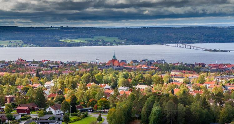 Panoramisch uitzicht op Östersund met kerktoren, stad aan het meer en lange brug onder dramatische wolken.
