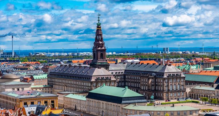 Een groots paleizencomplex met een hoge toren staat nabij de haven van Kopenhagen onder een bewolkte hemel.