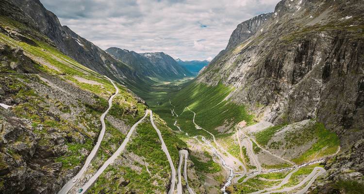 Dramatische Luftaufnahme der Trollstigen-Straße, die sich steile Bergwände hinauf in Richtung eines grünen Tals schlängelt.