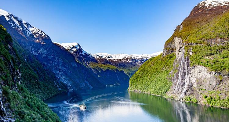 Kreuzfahrtschiff segelt durch den schmalen Geirangerfjord, flankiert von hoch aufragenden Klippen und Wasserfällen.