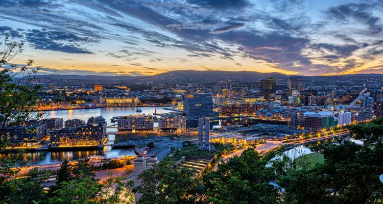 Sonnenuntergang-Panorama der Osloer Skyline mit leuchtenden Wolken und Spiegelungen im Hafen.