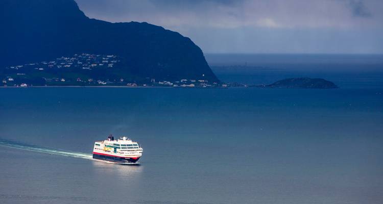 Passenger ferry cruising across calm blue sea with rugged coastline in the distance.