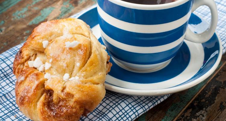 Nahaufnahme eines Zimtschnecke neben einer gestreiften Kaffeetasse auf einer rustikalen Tischdecke.