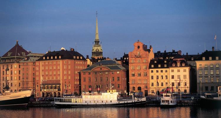 Paisaje urbano clásico de Gamla Stan de Estocolmo con edificios de colores pastel y campanario de iglesia al atardecer.