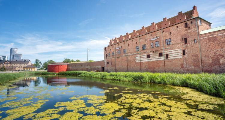 Castillo de ladrillo Malmöhus reflejado en un foso con el horizonte de la ciudad moderna al fondo.