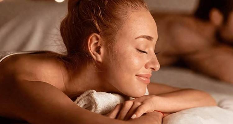 Primer plano de una mujer sonriente disfrutando de un masaje relajante en un ambiente de spa con iluminación suave.