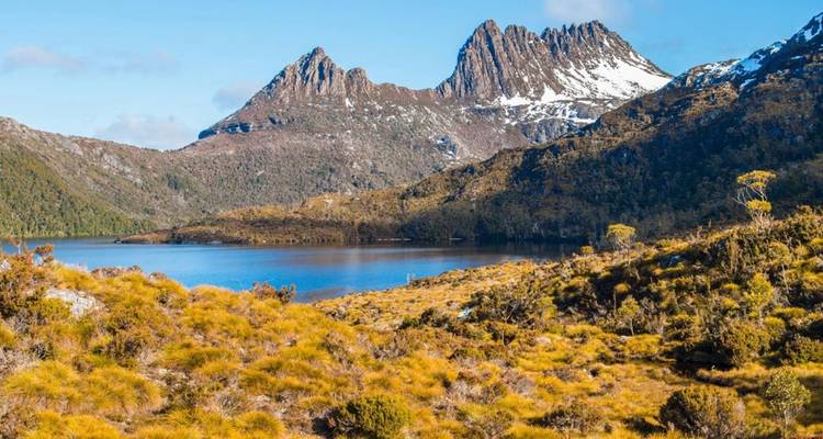 Le mont Cradle aux sommets enneigés s'élevant au-dessus d'un lac alpin calme et de plaines dorées de touffes d'herbe en Tasmanie