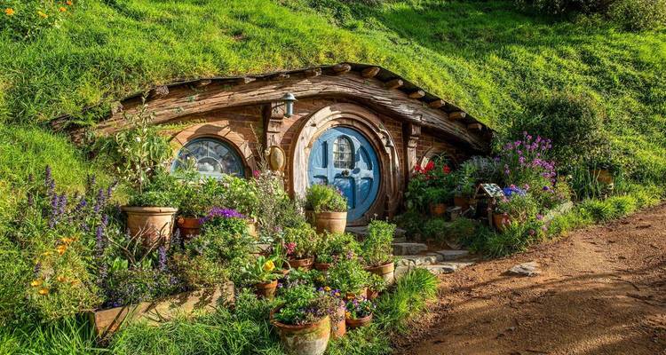 Encantadora casa hobbit con puerta redonda azul y macetas de flores vibrantes anidada en una ladera cubierta de hierba.