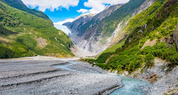 Valle que conduce al Glaciar Franz Josef entre montañas verdes empinadas y cielo azul