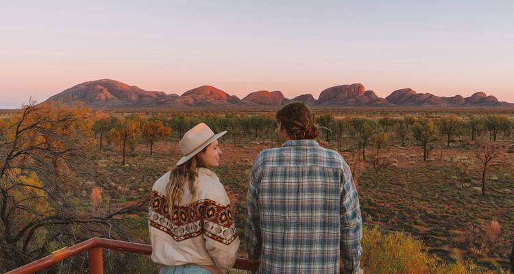 Couple admirant les reflets du coucher de soleil sur les dômes de Kata Tjuta à travers une vaste plaine désertique.
