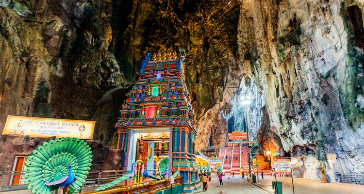 Farbenfroher Hindu-Schrein und Pfauenstatuen in einer riesigen Kalksteinhöhle mit einigen Besuchern, die entlang des Weges gehen.