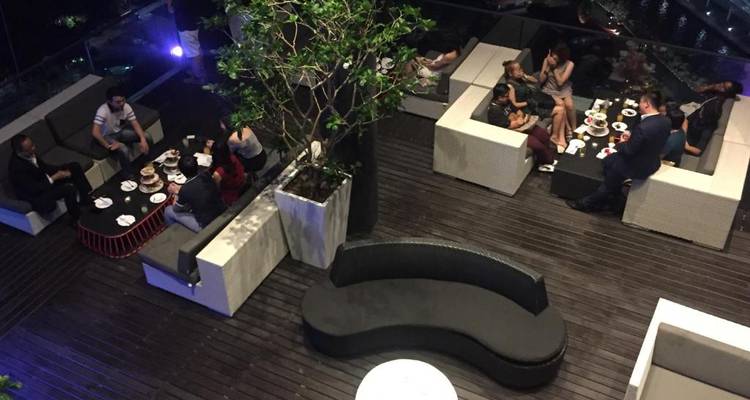 Vista aérea de huéspedes conversando y disfrutando de bebidas en un área moderna de lounge en la azotea por la noche.