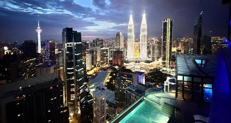 Paisaje urbano nocturno de Kuala Lumpur con las Torres Petronas iluminadas vistas desde una piscina infinita.