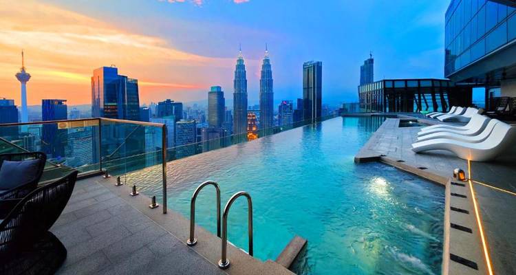 Los tonos del atardecer sobre una piscina infinita en la azotea con vistas al horizonte de Kuala Lumpur y las Torres Petronas.