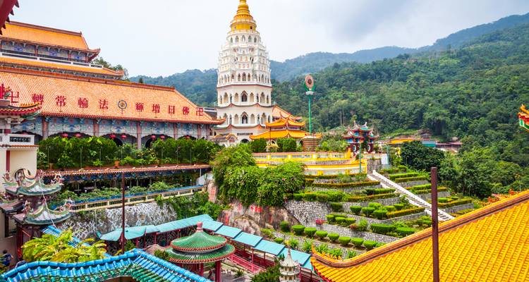 Templos coloridos y jardines en terrazas de Kek Lok Si con colinas boscosas de fondo.