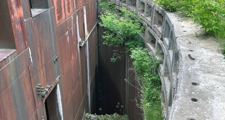 Pozo vertical estrecho entre muros oxidados de búnker con plantas creciendo desde las grietas