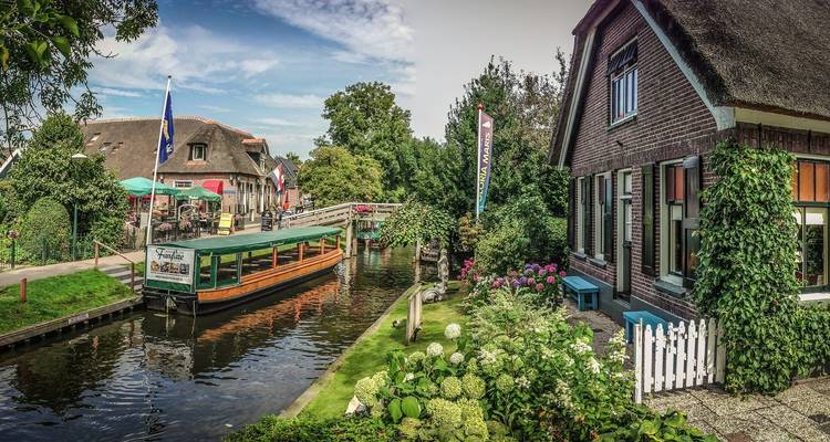 Pittoresk kanaalplaatsje met rondvaartboot, gewelfde houten brug en bloementuinen in Giethoorn